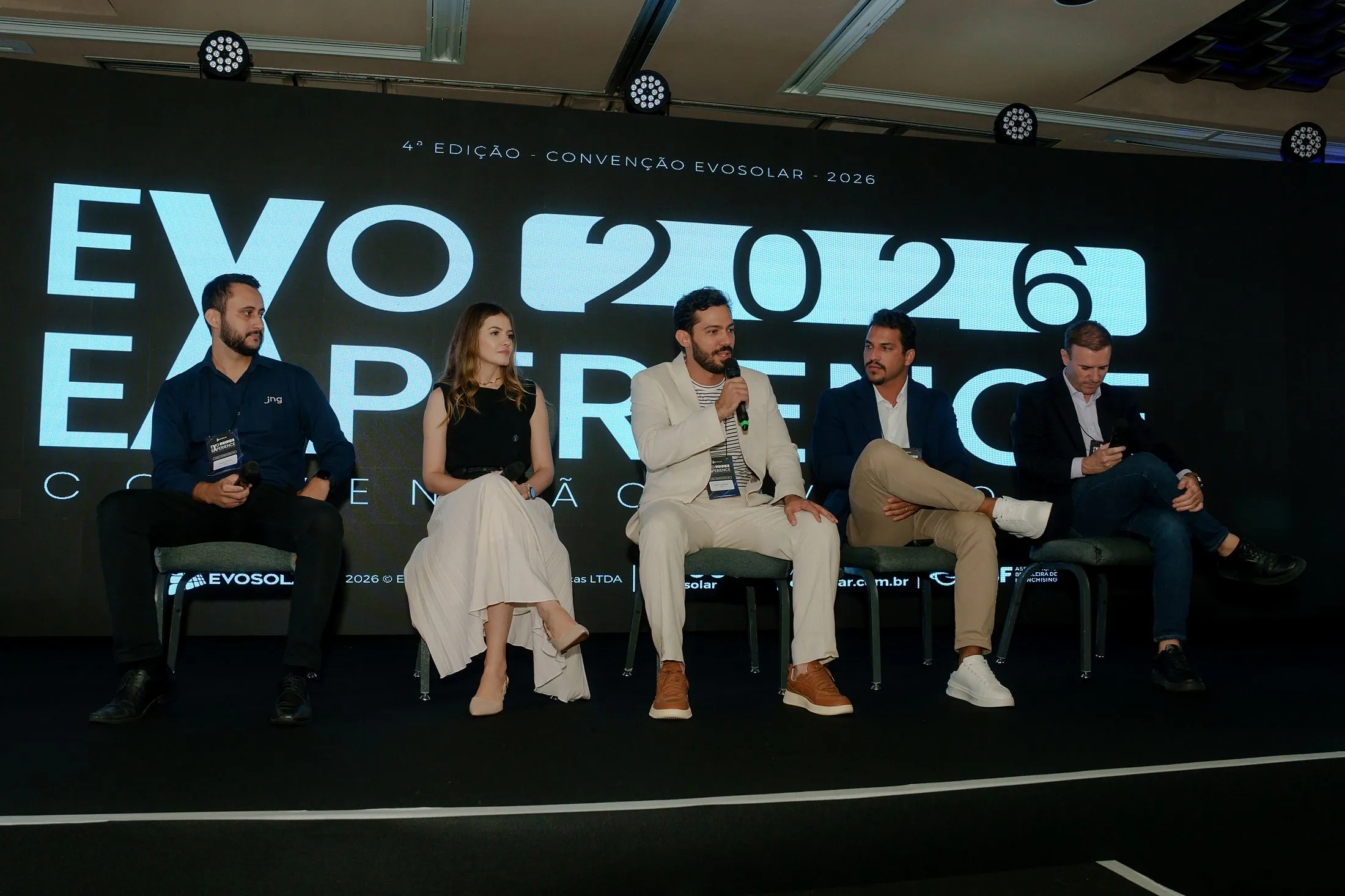 Os palestrantes sentados no palco da mesa redonda, sob o painel EVO 2026 EXPERIENCE
